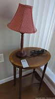 Side table with oval wooden top and wooden lamp base with striped fabric shade on top