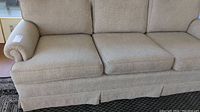 Front view of beige upholstered sofa with three seat cushions and skirted base on black and white rug.