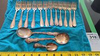 Twelve pastry forks arranged in row with two large spoons and one small spoon below on cloth