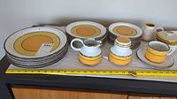 Full view of plate stacks, cup, creamer, sugar bowl and lidded dish on table with measuring tape