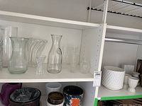 Glass vases clear and transparent different sizes and shapes on shelf with taller fluted vases and a carafe style vase