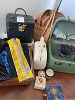 Photo showing multiple cosmetic bags including black hard case, light green vintage case, white woven handbag, wicker baskets behind, and small trinket boxes on floor.
