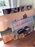 Six canvas prints arranged leaning against a wall, showing variety in size and subject including floral, architectural, beach scenes.