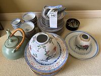 Wide view of the teapot, stacked plates, bowls, cups, and spoons showing overall lot contents
