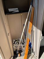 Wooden oars, grapple hook and variety of cleaning supplies in plastic bins in storage area