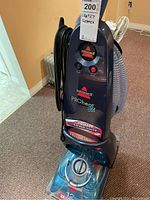 Upright Bissell ProHeat 2X carpet cleaner showing full unit from front with cord wrapped on side and water tank visible.