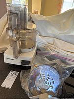 Overall view of Cuisinart Classic food processor with bowl, lid, and discarded stainless steel discs in plastic bags on counter surface.