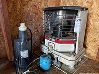 Photo showing the Sharp kerosene heater next to the Star submersible pump with visible control and protective cage on the heater.