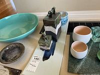 Photo showing assortment of bowls, containers, and dishes arranged on a rug with wood floor background, includes price tag.