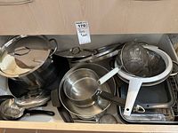 Various stainless steel pots, strainers, roasting pan stacked in cabinet