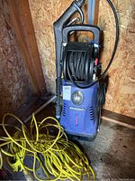 Full front view showing Simoniz power washer with yellow extension cord attached on floor.