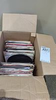 Box of assorted 45 RPM vinyl records with paper sleeves, viewed from above