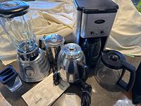 Photo showing Cuisinart coffee maker, blender with glass jar, electric kettle, and a small plastic accessory along with instruction manual.
