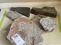 Seven flat stone pieces of various colors and sizes displayed on carpet, showcased to illustrate the lot contents. One stone is pink granite with a Moosad tag showing 15 1/2 inches dimension.