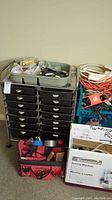 Two metal storage units with multiple drawers, a gray tray with tools on top, orange and white extension cords, and a red tool bag at the base