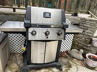 Full front view of BroilMate Signet gas BBQ grill with side shelves and wheels, set outdoors on stone patio.
