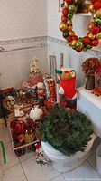 Photo showing assorted Christmas village accessories, tins, candles, plush snowman, and a wreath on the toilet seat