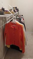 Clothing rack showing several colorful jackets and tops, with an orange button-up jacket in front.