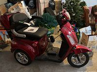 Right-side view of metallic red three-wheeled scooter with padded seat and storage trunk