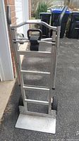 Front view of aluminum dolly standing upright showing platform and handles.