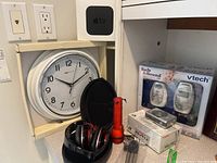 Photo of all items including wall clock, headphones inside case, flashlight, baby monitor box, stacked boxes, and Apple TV box on shelf.