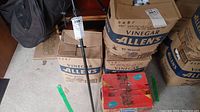 Two upright Allen's vinegar branded boxes stacked behind a red Domingo juice box containing golf balls.