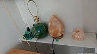 Wide view of two lamp bases on a shelf: a green ceramic lamp base with floral design and a Himalayan salt lamp candle holder with rough texture.