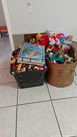Two bins filled with assorted Lego pieces and one containing toys including stuffed animals, placed on a tiled floor.
