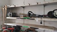 Wide view of shelf holding the electric hedge trimmer, saw blades, and other items