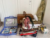 Complete view of all items: wooden sewing box, stack of fabric, blue plastic case with jewelry making supplies, and basket with craft materials.