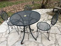 Photo showing round metal mesh outdoor table with three metal mesh chairs arranged around it on a stone patio. Weathered condition visible.