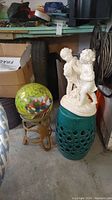 View of all three items: glass ball on metal stand, ceramic table/stool, white resin figurine of two children