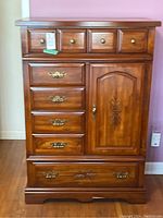 Front view of wood armoire showing top small drawers, middle stacked drawers, side door, and bottom drawer.