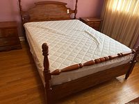Full view of queen size wooden bed frame with mattress topper, showing headboard, footboard, posts, and one nightstand on side.