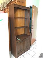 Front view of the wooden bookcase showing three shelves and the base cabinet with paneled doors.