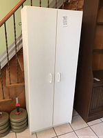 Closed white pressed wood cabinet showing two doors and plastic handles