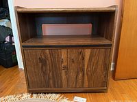 Front view of medium-dark wood cabinet closed showing pull-out shelf and double-door storage.