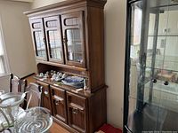 Wooden china cabinet from an angled front view, showing upper glass doors and lower storage with decorative hardware.
