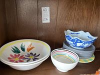 Ceramic bowls and plates arranged on shelf, showing different sizes and patterns including floral designs and blue and white scalloped bowl on gray plates.