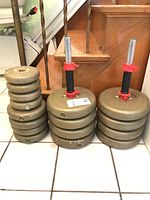Photo showing multiple stacks of beige York Barbell dumbbell plates and two dumbbell bars with red locking collars.