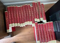 Photo showing all volumes of The Illustrated Columbia Encyclopedia arranged on a hardwood floor, showing red and cream colored spines with gold text.