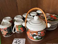 Front view of the covered pot with handle, surrounded by 8 espresso cups and stacked small plates.