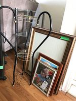 Four photo frames of varying sizes leaning against wall next to black metal plant stand with three circular shelves