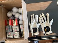 Box with mixed golf balls and two white Callaway Warbird golf gloves with black detailing