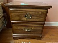 Close-up photo showing one wooden night table with two drawers and brass handles.