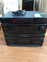 Stacked Pioneer stereo components on wooden floor with power cable coiled on top. Visible model numbers on front panels of each unit.