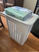 White plastic laundry hamper with rectangular side vents and lid, sitting on wooden floor.