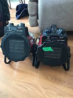 Two compact space heaters side by side, showing front metal grills and control knobs on top.