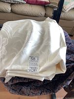 Cream/off-white damask fabric folded with floral pattern visible, labeled 6.5x2, 5x2, 4x5 with upholstery fabric tag.