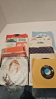 Array of 12 mixed 45 RPM vinyl records in their original sleeves of various labels including Polydor, WEA, and RCA